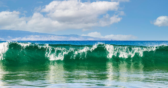 Breaking wave and surf rolling into the shore at D.T. Fleming Beach with a view of the Island of Molokai in the distance; Kapalua, Maui, Hawaii, United States of America