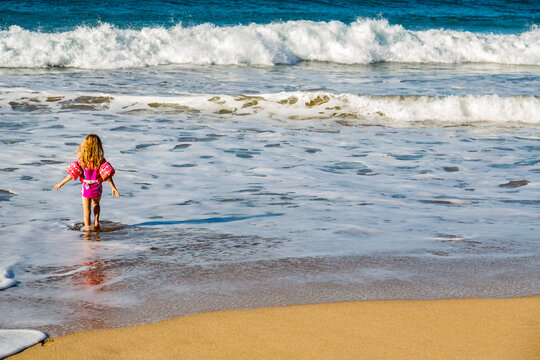 View taken from behind of a young girl walks from the beach into the ocean water as the waves roll into shore at D.T. Fleming; Kapalua, Maui, Hawaii, United States of America