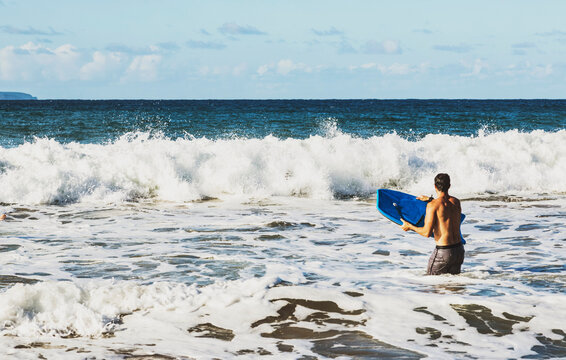 View taken from behind of a man stands in the ocean holding a bodyboard waiting to catch a wave at D. T. Fleming Beach; Kapalua, Maui, Hawaii, United States of America