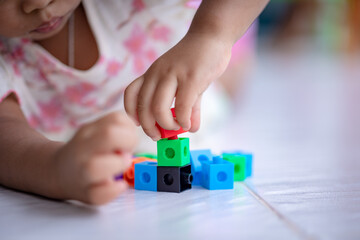 Girl is using hands assembling colored cubes in child development builder concept.