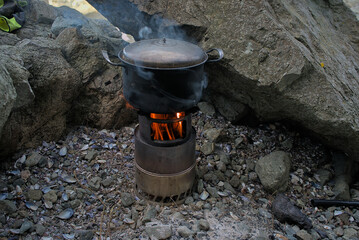 Wood burner for cooking outdoors in the wild. Surrounded by stones, food is cooked in a pot on a...