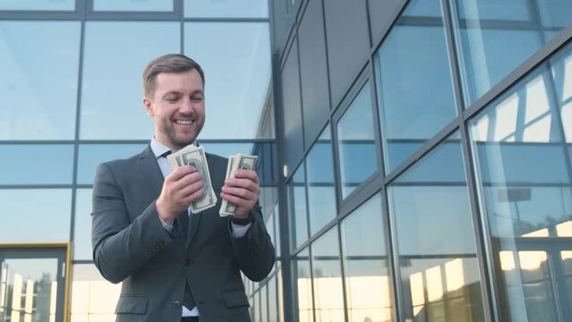 An attractive young man on the background of a skyscraper holds US dollars in his hands. 