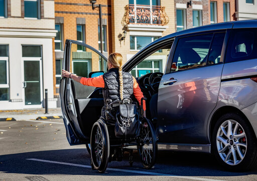 Young paraplegic woman moves from her wheelchair to the driver's seat of a car in a parking lot; Edmonton, Alberta, Canada