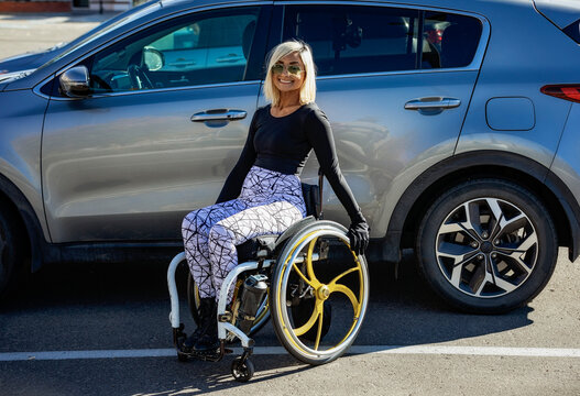 Young paraplegic woman in her wheelchair outside her adapted vehicle in a parking lot; Edmonton, Alberta, Canada