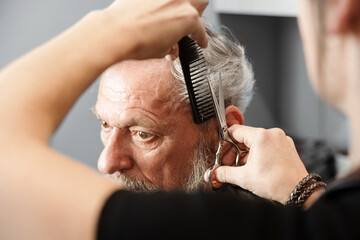 Closeup hands working with hair scissors. Professional hairstyler woman cutting hair of mature man....