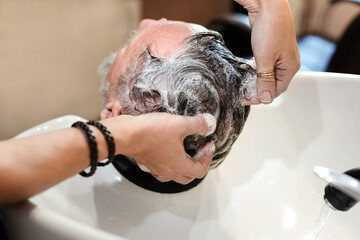 Foam of shampoo on head. Professional woman hairstyler wash hair of mature man at barbershop or...