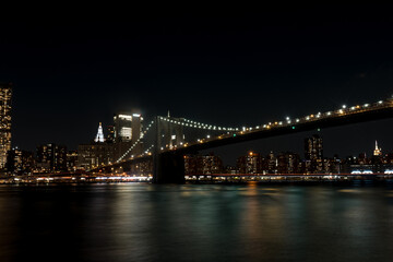 Fototapeta na wymiar Brooklyn Bridge in New York at night. Skyscrapers of a large metropolis. Night city at long exposure. Towers in the big city.