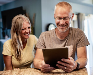 Mature couple sitting a home laughing together at content on a tablet; Edmonton, Alberta, Canada