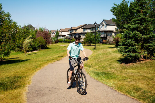 Young man riding his bike down a path in a residential park; Edmonton, Alberta, Canada