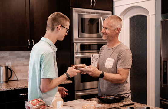 Young man serving his dad a sandwich in the kitchen at home; Edmonton, Alberta, Canada