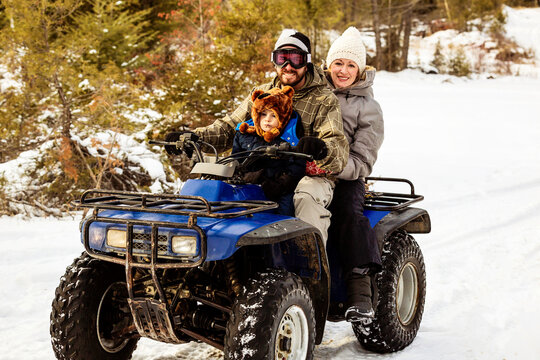 A Man and Woman Riding An ATV With A Young Boy On A Snowy Trail In Winter At A Mountain Resort; Fairmont Hot Springs, British Columbia, Canada