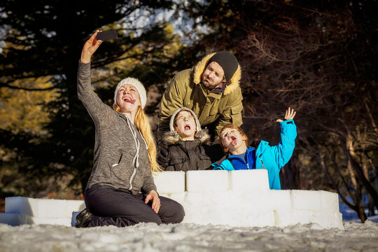 A Mother Takes A Self-Portrait Of Their Family Making Crazy Faces While Building An Igloo Together Out Of Snow Blocks At A Mountain Resort; Fairmont Hot Springs, British Columbia, Canada