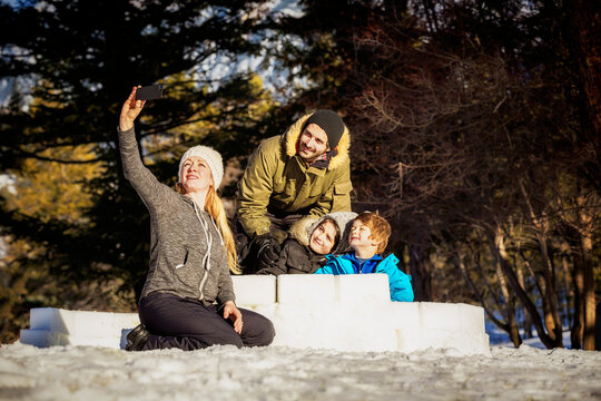 A Mother Takes A Self-Portrait Of Their Family Building An Igloo Together Out Of Snow Blocks At A Mountain Resort; Fairmont Hot Springs, British Columbia, Canada