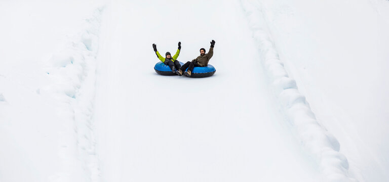 Father and son tubing down a ski hill in tandem; Fairmont Hot Springs, British Columbia, Canada