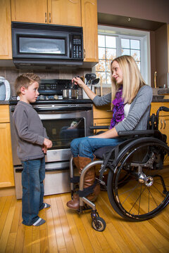 Young disabled woman talking with her young son while cooking in the kitchen at home; Spruce Grove, Alberta, Canada