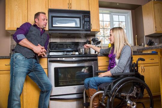 Husband and wife, who has a disability and is in a wheelchair, having a discussion in their kitchen while she is cooking; Spruce Grove, Alberta, Canada