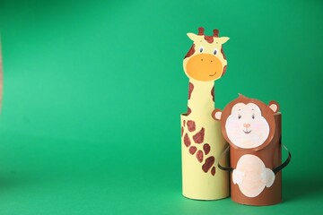 Toy monkey and giraffe made from toilet paper hubs on green background, space for text. Children's handmade ideas