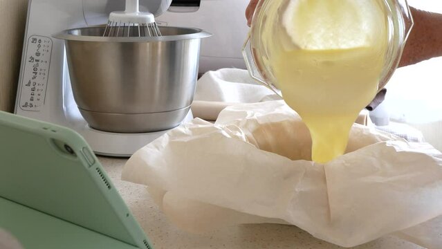Filling mold with batter before the baking. Batter is poured into round cake mold covered with baking paper, selective focus. Making cake or pie according online cooking class