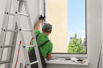 Worker in uniform installing double glazing window indoors, back view