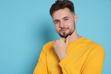 Obraz premium Handsome man in yellow sweatshirt on light blue background, space for text