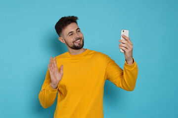 Handsome man in yellow sweatshirt with phone on light blue background