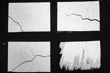 Four torn sheets of white paper on a black wall.