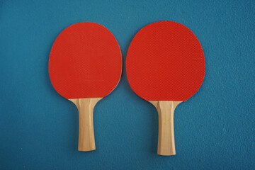 Two red table tennis or ping pong rackets lie on a blue background with a close-up view from above....
