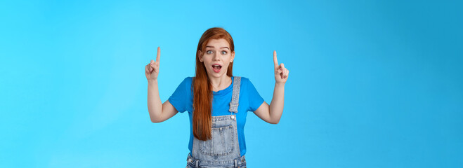 Excited cheerful cute ginger girl 20s, open mouth entertained, look enthusiastic amazed, pointing...