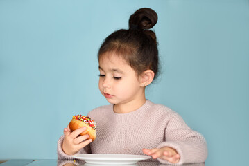 Portrait of a smiling charming little girl eating donuts decorated with chocolate icing, cream, and...