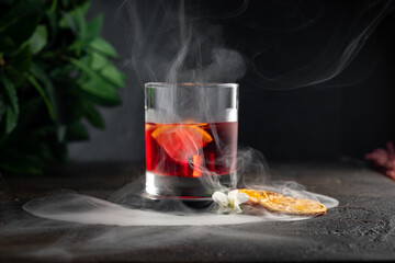 Smoked old-fashioned rum cocktail with ice cubes, lemon and flowers. Alcoholic cocktail in a glass