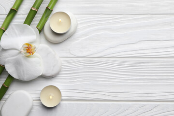 Bamboo stems, orchid, spa stones and burning candles on white wooden table, flat lay. Space for text