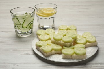Tasty sandwiches with butter and cucumber served on white wooden table