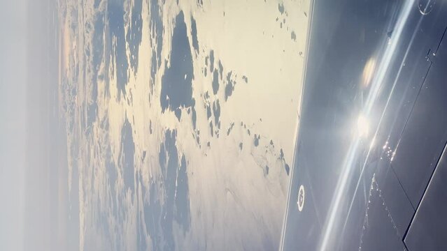 Vertical footage through illuminator of the wing of the Scandinavian airlines aircraft when landing in clear sunny weather, clouds, islands in the sea