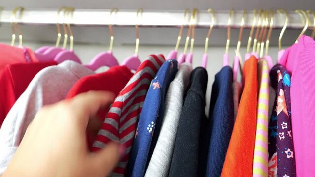 A woman's hand hangs a blouse in a wardrobe. Lots of bright teenage clothes on pink hangers in the closet. Putting things in order.