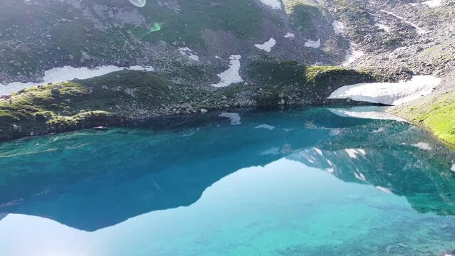Quadrocopter shoot to blue lake between high mountains in the wild nature. The beautiful view from sky with drone