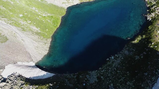Quadrocopter shoot to blue lake between high mountains in the wild nature. The beautiful view from sky with drone