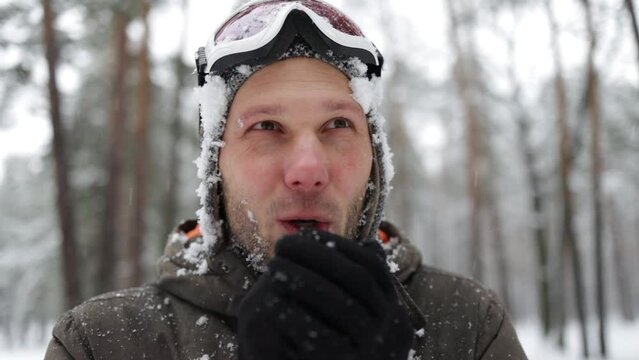 An adult brutal man with a beard in a winter forest all face in the snow. Man shivering in cold winter and rubbing hands until snow.