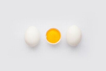 Whole chicken Eggs and cracked half with raw yolk on white background. Minimalism