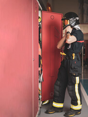 A young firefighter removing his uniform in front of a locker inside the fire station.