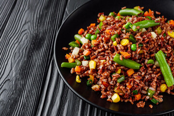 delicious red rice with vegetables on a black wooden rustic background