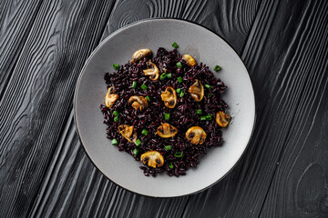 delicious black rice with mushrooms on a black wooden rustic background