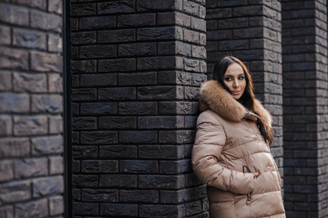 Beautiful young pregnant woman in a brown coat, in the background a brick wall