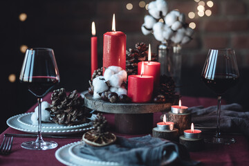 Rustic table decor for Christmas or New Year family dinner. Centrepiece with red candle, dry orange, cone, cinnamon, anise. Zero waste eco-friendly home. Cozy atmosphere, dark background. Close up