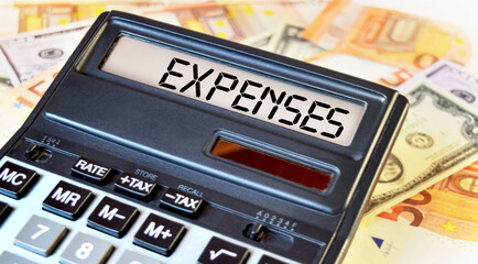 EXPENSES text written on a calculator next to the background of euro banknotes. Finance or business concept.