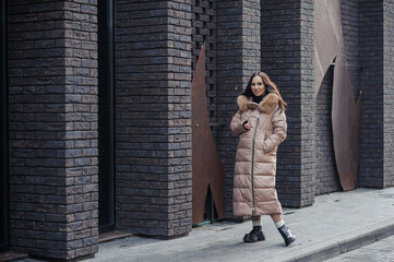 Fototapeta na wymiar Beautiful young pregnant woman in a brown coat, in the background a brick wall