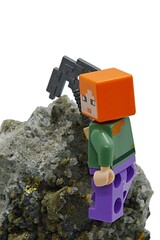 Fototapeta premium LEGO Minecraft figure of Alex with iron pickaxe mining Chalcopyrite mineral rock, white background. 