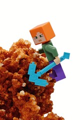 Fototapeta premium LEGO Minecraft figure of Alex climbing on orange Calcite mineral rock with diamond pickaxe, white background. 