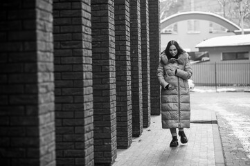 Beautiful young pregnant woman in a brown coat, in the background a brick wall