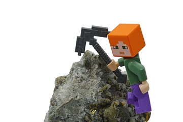 Fototapeta premium LEGO Minecraft figure of Alex with iron pickaxe trying to mine Chalcopyrite mineral rock, white background. 