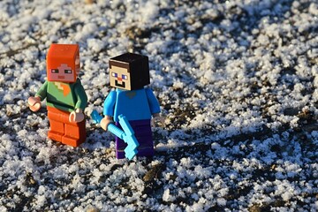 Fototapeta premium LEGO Minecraft figures of Steve and Alex on a walk on dirt road covered with first flakes of snow, morning sunshine. Steve is holding diamond pickaxe